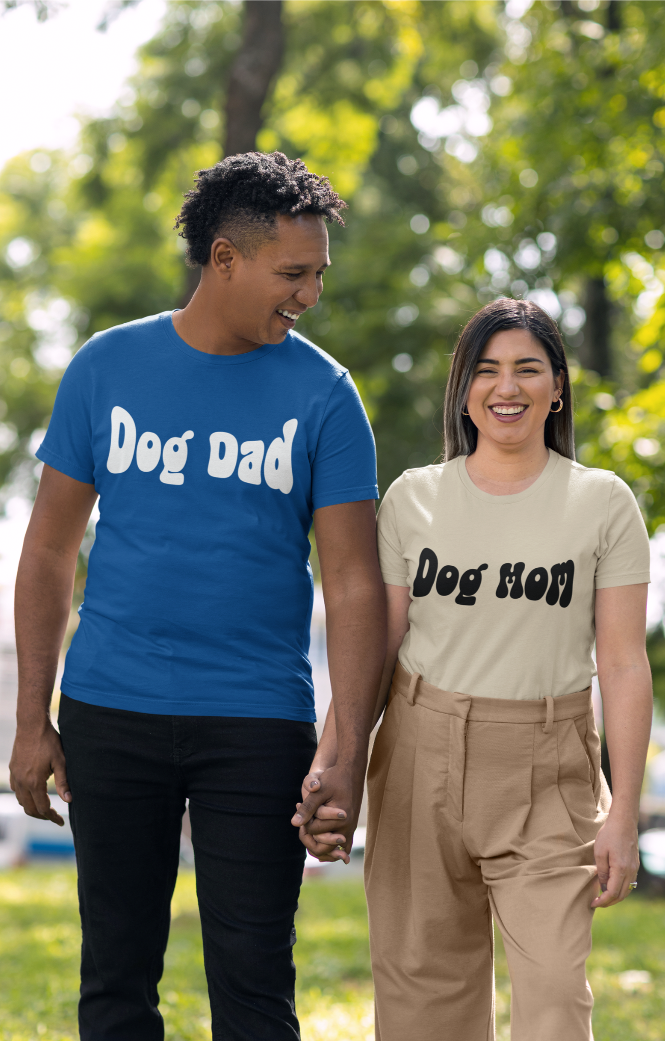 Two people walking outdoors, one wearing a blue 'Dog Dad' shirt and the other in a beige 'Dog Mom' shirt.